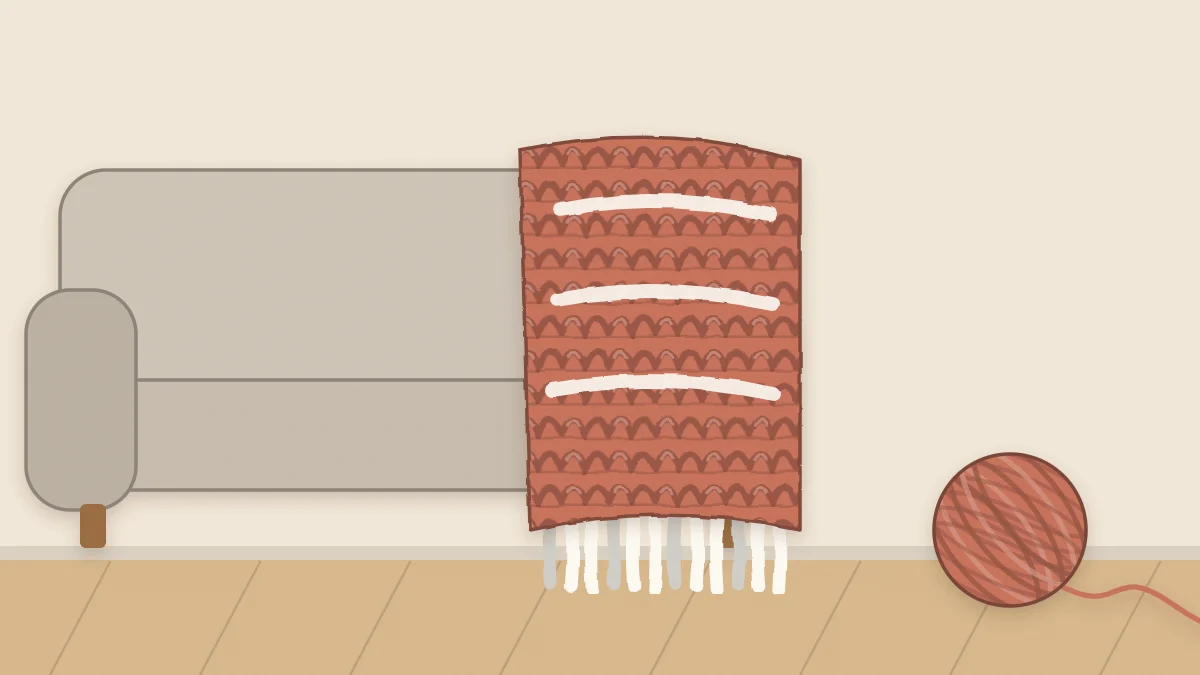 A folded chunky crochet throw blanket draped over the arm of a sofa
