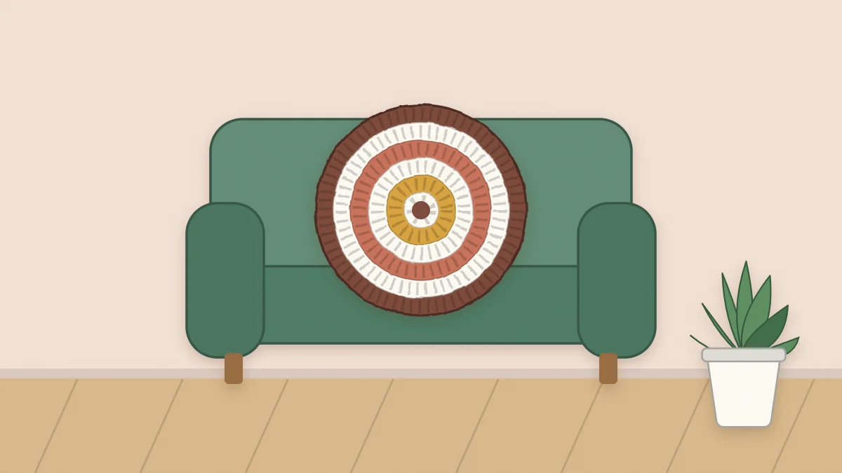 A round crochet cushion with concentric rounds sitting on an armchair